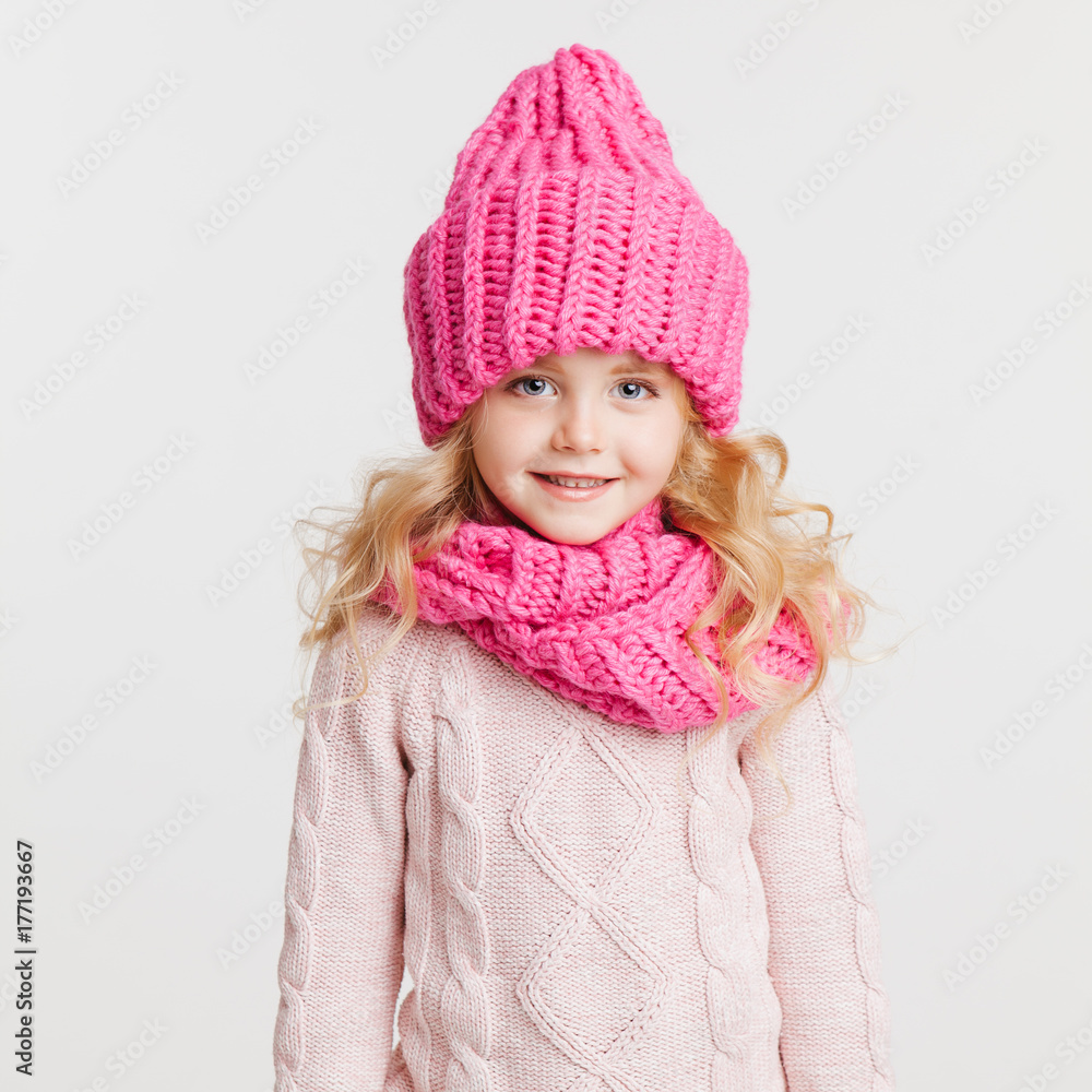 Winter clothes. Portrait of little curly girl in knitted pink winter hat and scarf Winter clothes. Portrait of little curly girl in knitted pink winter hat and scarf
