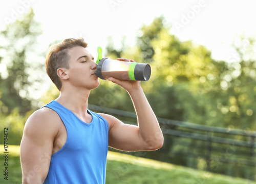 Sporty young man drinking protein shake outdoors