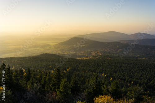Sunset foggy landscape with hills and clear blue sky with yellow shine from the sun.