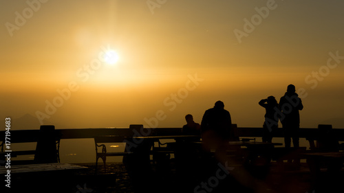 Hot yellow sky dusring sunset. Silhouette of people sitting on bench.