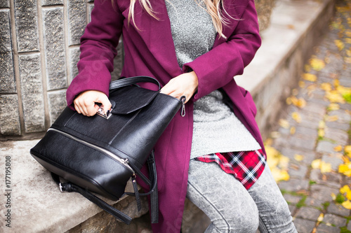A girl in a purple coat with a black handbag. Close-up. Female style of street fashion in casual style.
