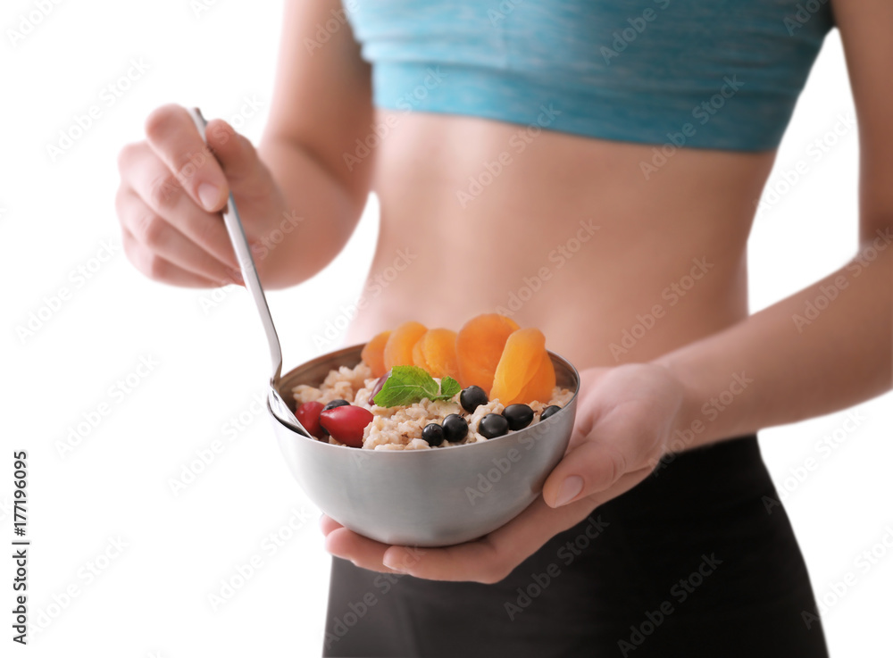 Sporty woman holding spoon and bowl with nutritious oatmeal on white background Sporty woman holding spoon and bowl with nutritious oatmeal on white background