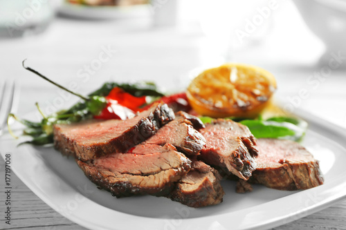 Plate with sliced delicious steak and vegetables on table