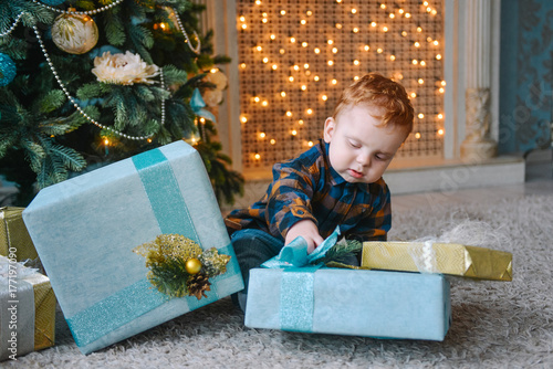 little boy sitting near boxes and opening Christmas presents photo