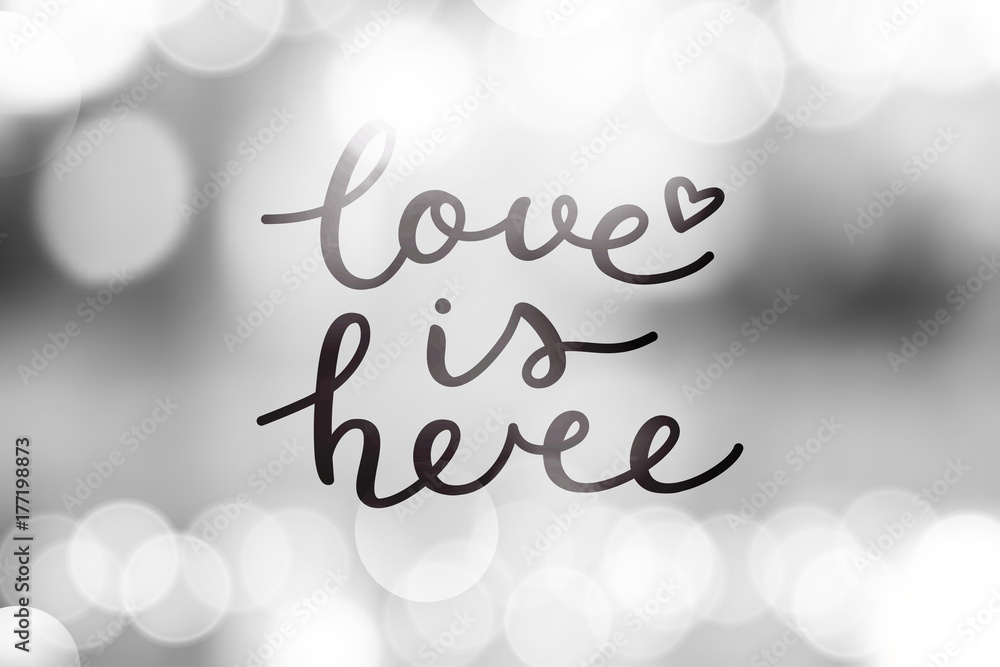 love is here lettering, vector handwritten text on blurred lights