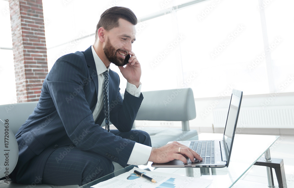 Businessman talking on smartphone and typing text on laptop