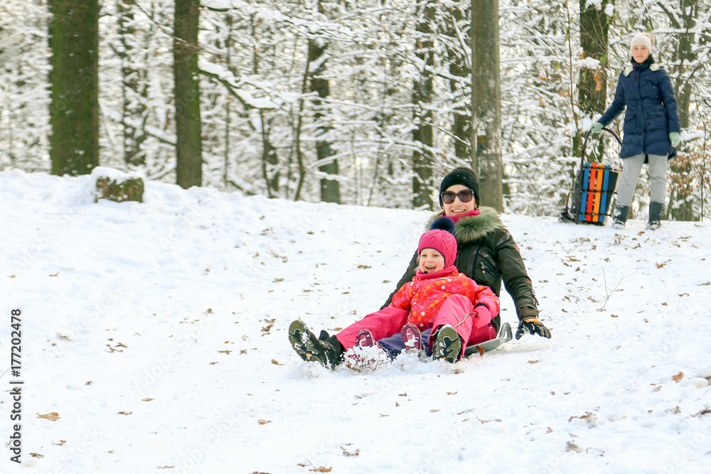 Beautiful sporty caucasian girl with daughter having fun and sledding in a forest or city park on a bright sunny day. Winter family activity concept Beautiful sporty caucasian girl with daughter having fun and sledding in a forest or city park on a bright sunny day. Winter family activity concept