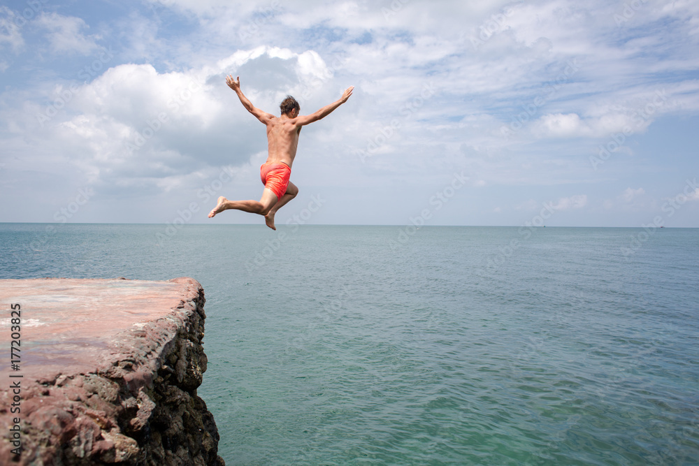 Summer fun - man jumping off cliff into the ocean Summer fun - man jumping off cliff into the ocean