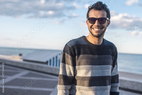 smiling handsome  Arabic young man in striped sweater on the sea coast, sunset,beach,clouds photo