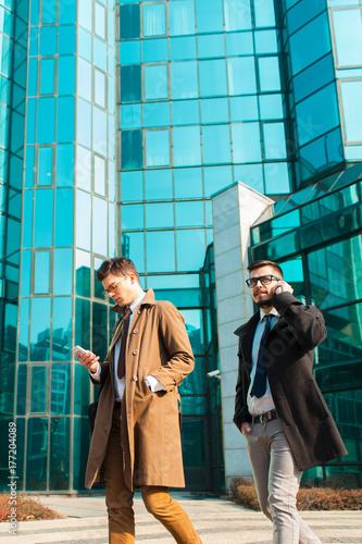 Two stylish businessmen walking in front of corporative building.