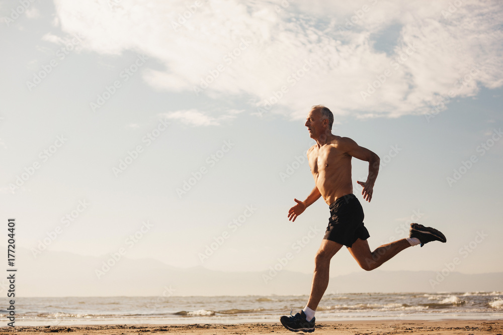 Active senior man - in great shape - running shirtless on beach in morning sunshine Active senior man - in great shape - running shirtless on beach in morning sunshine