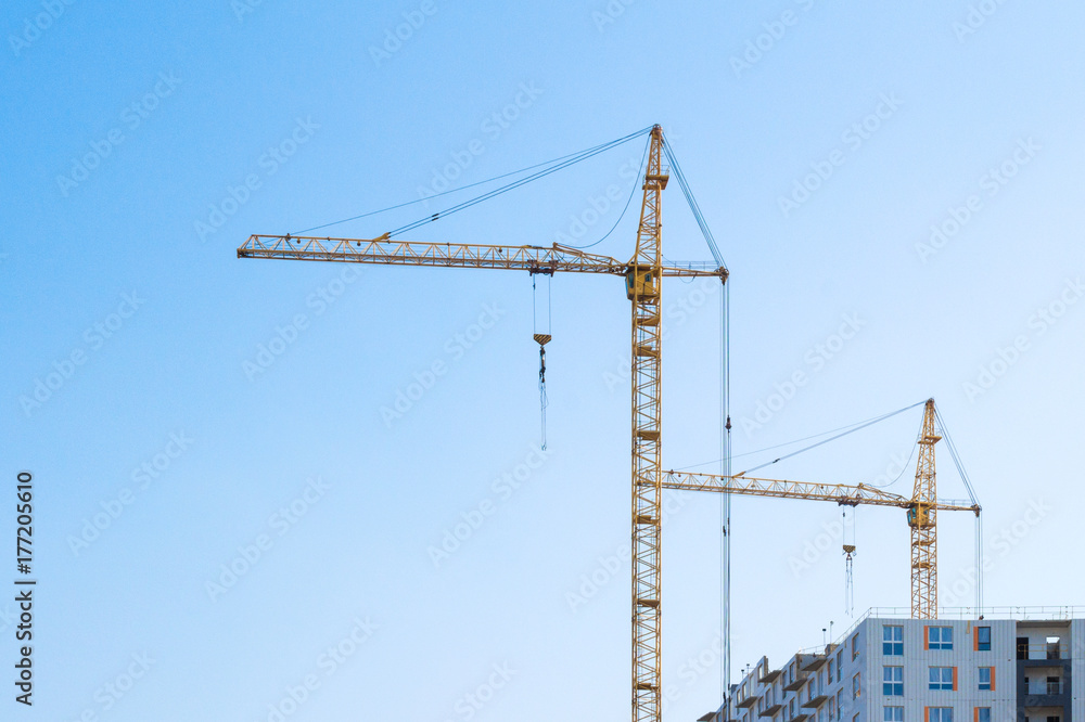 Construction cranes against the blue sky. Home buildings