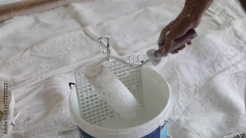 Close up slow motion of draining paint roller in bucket in renovation room with whitewasher