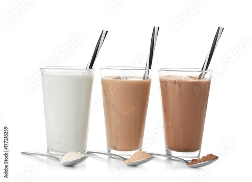Glasses with different protein shakes and powders in spoons on white background