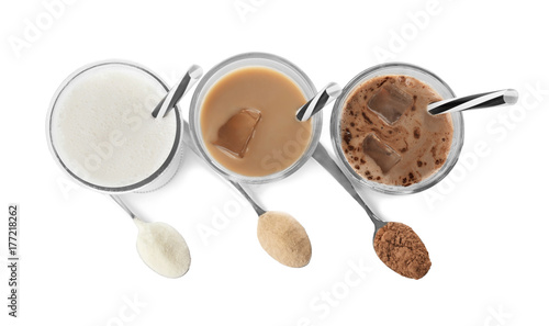 Glasses with different protein shakes and powders in spoons on white background