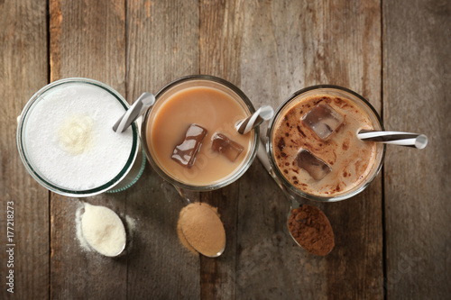 Glasses with different protein shakes and powders in spoons on wooden table