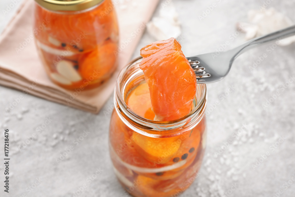 Fork and jar with delicious marinated salmon on table Fork and jar with delicious marinated salmon on table