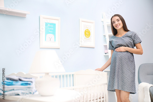 Pregnant woman standing near baby crib at home