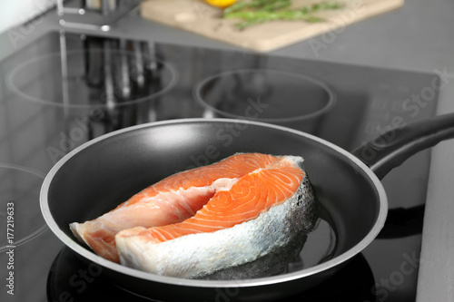 Frying pan with raw salmon steak on stove in kitchen