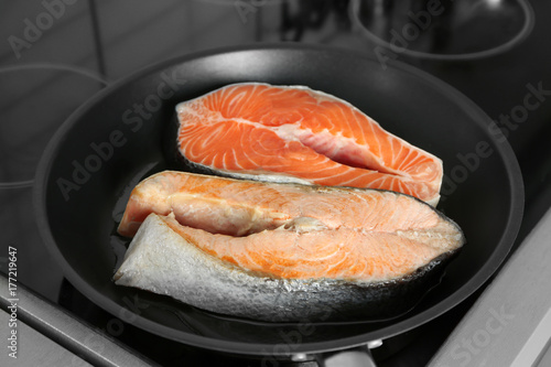 Frying pan with salmon steaks on stove in kitchen