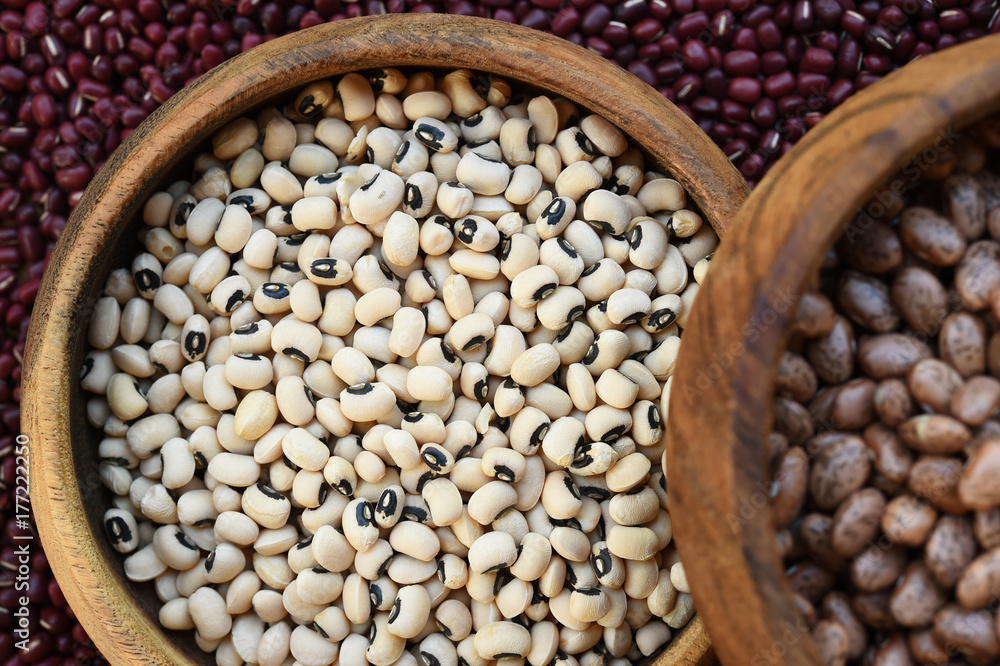 Black eyed peas and pinto bean in wooden bowl on red bean background Black eyed peas and pinto bean in wooden bowl on red bean background