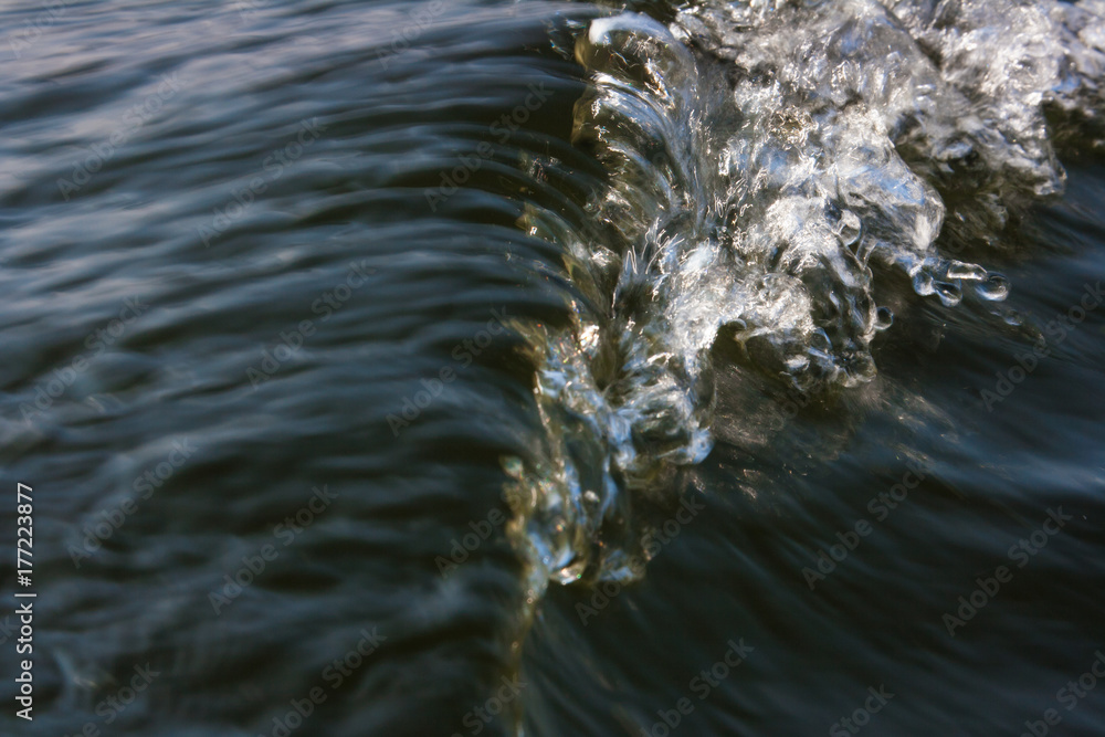 The water behind the stern of the boat.
Horizontally. White water breakers from the propeller of a motor boat with sunlight reflection.
