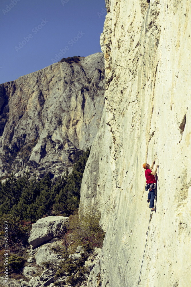 Young man climbs on a rocky wall in a valley with mountains.