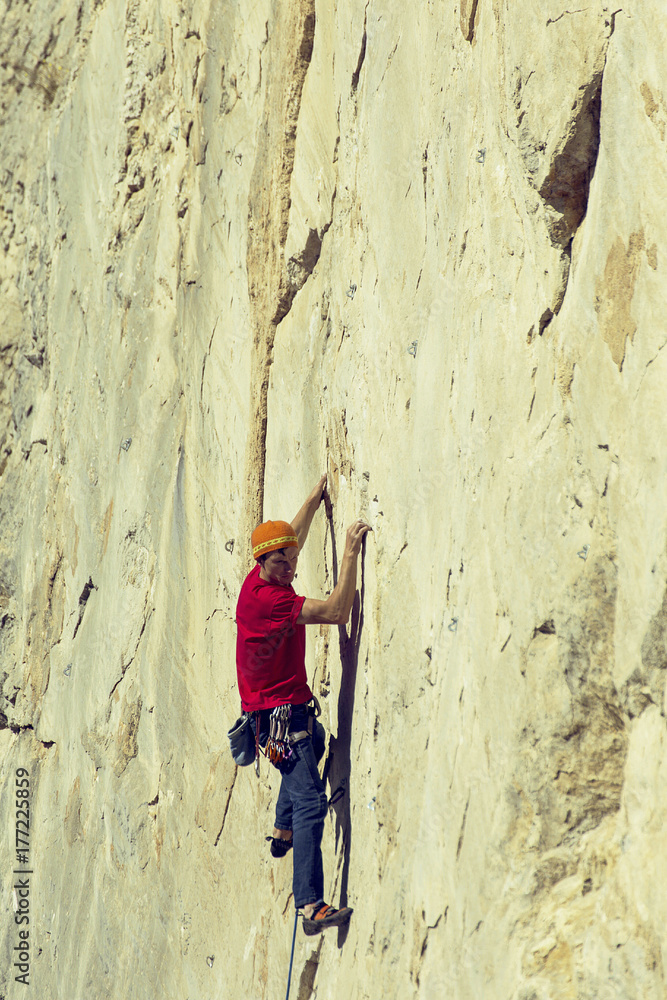 Young man climbs on a rocky wall in a valley with mountains. Young man climbs on a rocky wall in a valley with mountains.