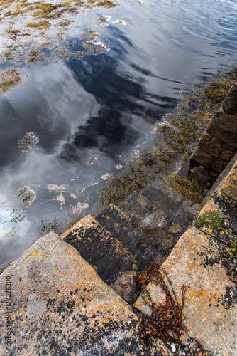 near the stairs of a stone pier, clouds are reflected in the waters of a small port of Connemara in Ireland.