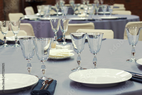 Preparation for a wedding banquet. The tables are covered with lilac tablecloth. Wine glasses are on the tables in the restaurant.