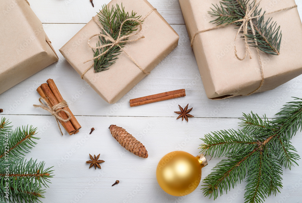 Christmas background with gift boxes wrapped in kraft paper, fir tree branches, golden glass balls, pine cones, cinnamon sticks and stars anise on white wooden background. Flat lay, top view Christmas background with gift boxes wrapped in kraft paper, fir tree branches, golden glass balls, pine cones, cinnamon sticks and stars anise on white wooden background. Flat lay, top view