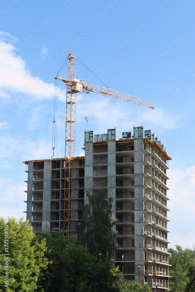 Tall crane works near tall residential building on construction site at summer day Tall crane works near tall residential building on construction site at summer day