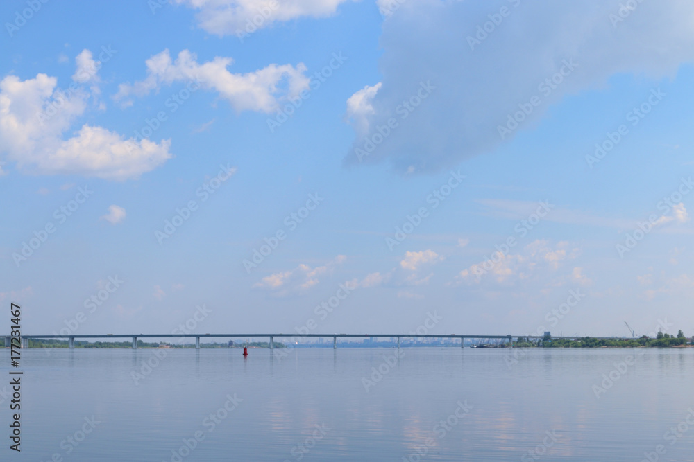 View of river and shore with bridge in distance on sunny summer day