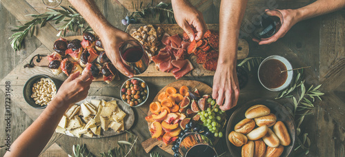 Flat-lay of friends hands eating and drinking together. Top view of people having party, gathering, celebrating together at wooden rustic table set with different wine snacks and fingerfoods
