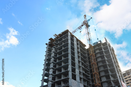 Concrete residential building under construction and crane at sunny day, under view