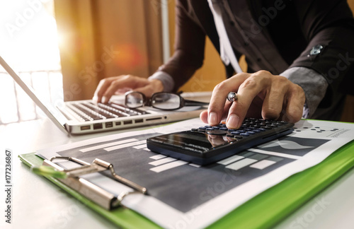 businessman hand working with finances about cost and calculator and laPtop with tablet and smartphone on withe desk in modern office in morning light 