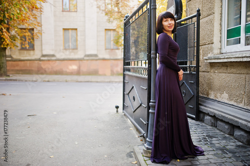 Adult brunette woman at violet gown background black iron gates. © AS Photo Family