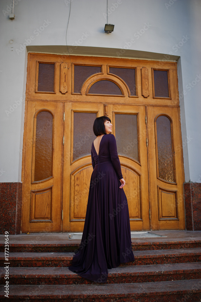 Adult brunette woman at violet gown background old wooden doors.