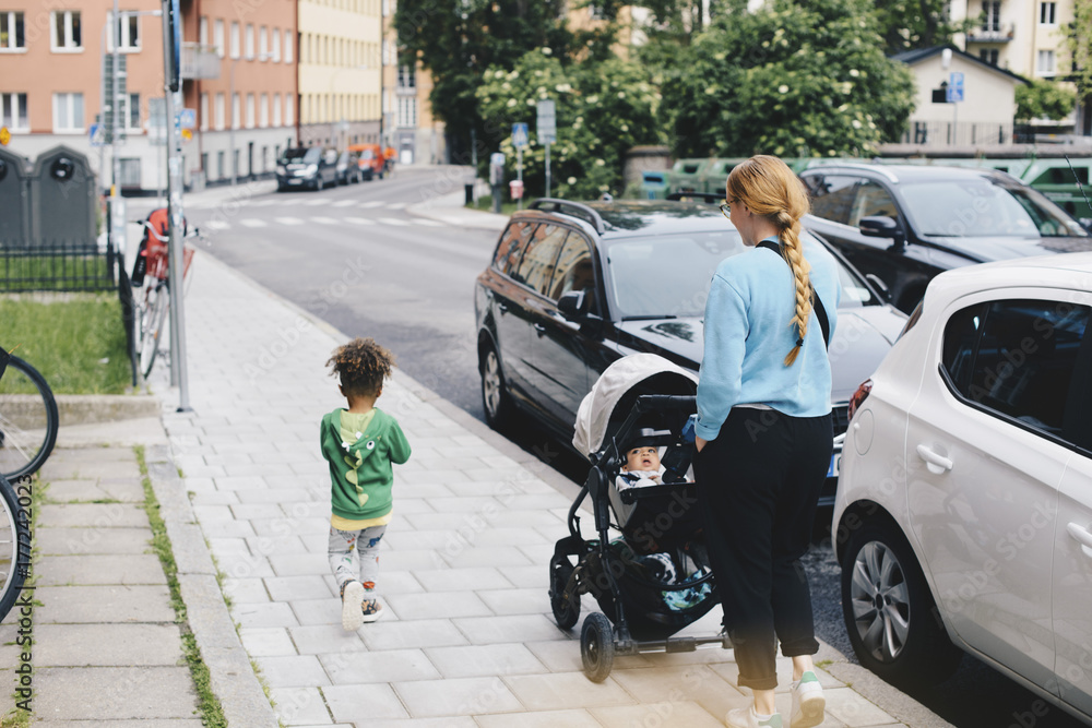 Mother pushing baby stroller while walking with son on sidewalk at city(02)