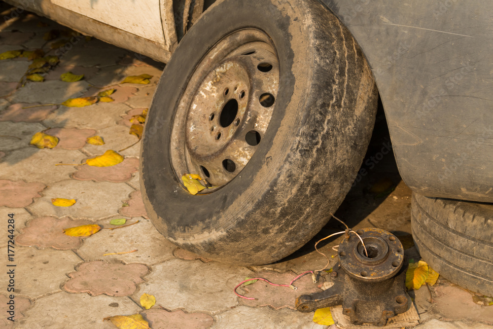 Old wheel near a white car for repair Old wheel near a white car for repair