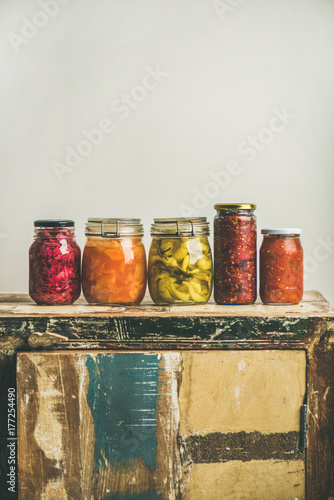 Autumn seasonal pickled or fermented vegetables in jars placed in line over vintage rustic kitchen drawer, white wall background, copy space. Fall home food preserving or canning
