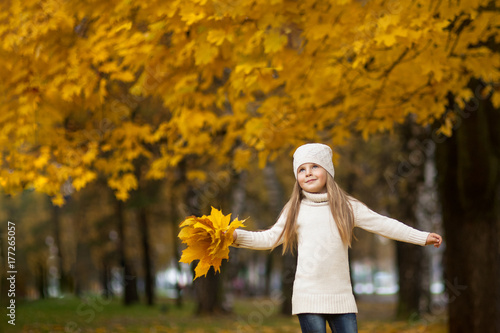 little girl with a maple leaf in her hands. in a light sweater and hat