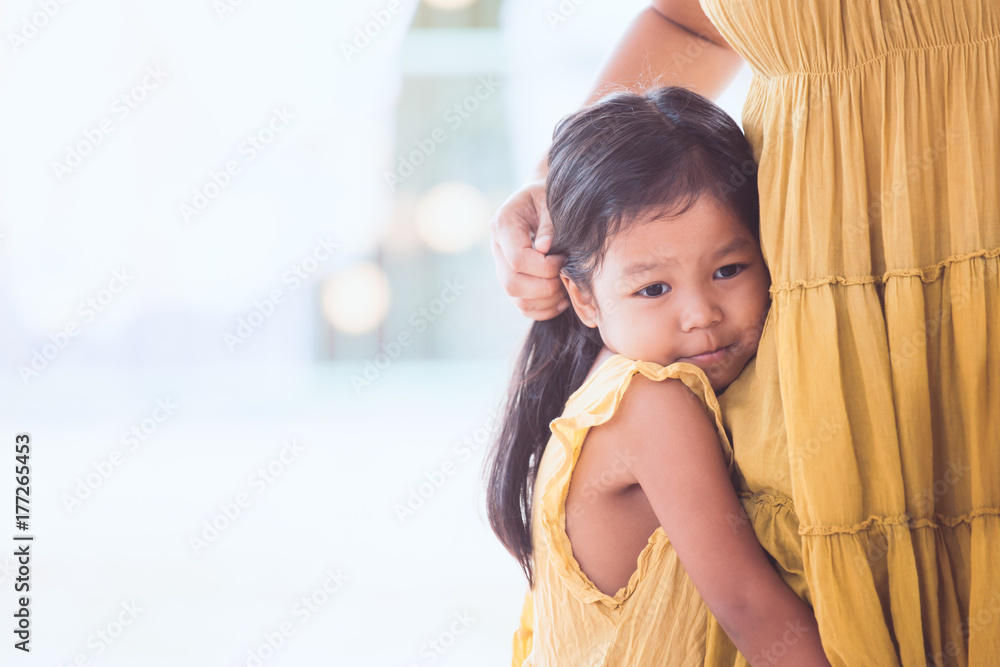 Sad asian child girl hugging her mother leg in vintage color tone Sad asian child girl hugging her mother leg in vintage color tone