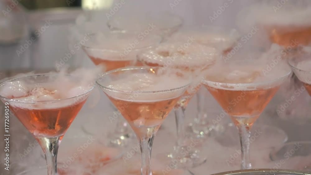 Feast alcohol. Close-up of shelf of glasses with seething martini and wine with dry ice. Man's hand takes a glass of wine Feast alcohol. Close-up of shelf of glasses with seething martini and wine with dry ice. Man's hand takes a glass of wine