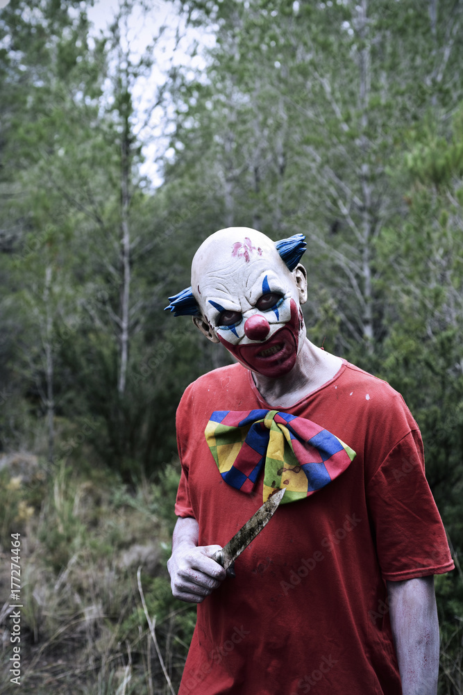 scary evil clown with a knife in the woods