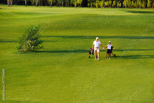 man with his son golfers walking on perfect golf course at summer evening