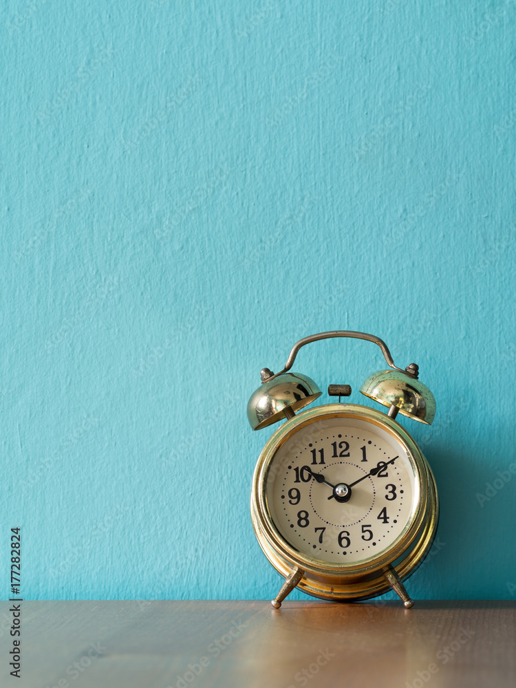 Gold vintage alarm clock on the wood table. the background is blue and copy space for text