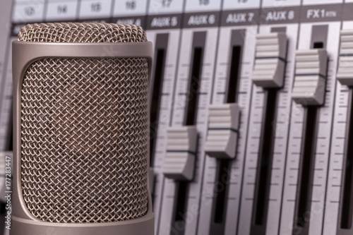 Professional recording microphone with studio audio mixer in the background.