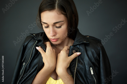 Tender young woman envelopes herself in leather jacket photo
