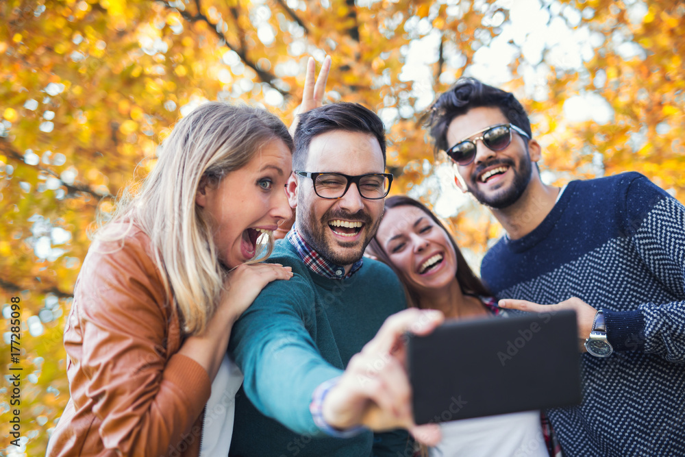 Group of four funny friends taking selfie with a smart phone in park Group of four funny friends taking selfie with a smart phone in park